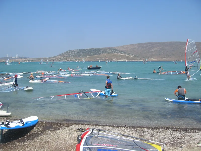 Alaçatı Çark plajında rüzgar sörfü yapanlar ve kıyıdaki board ile yelkenler