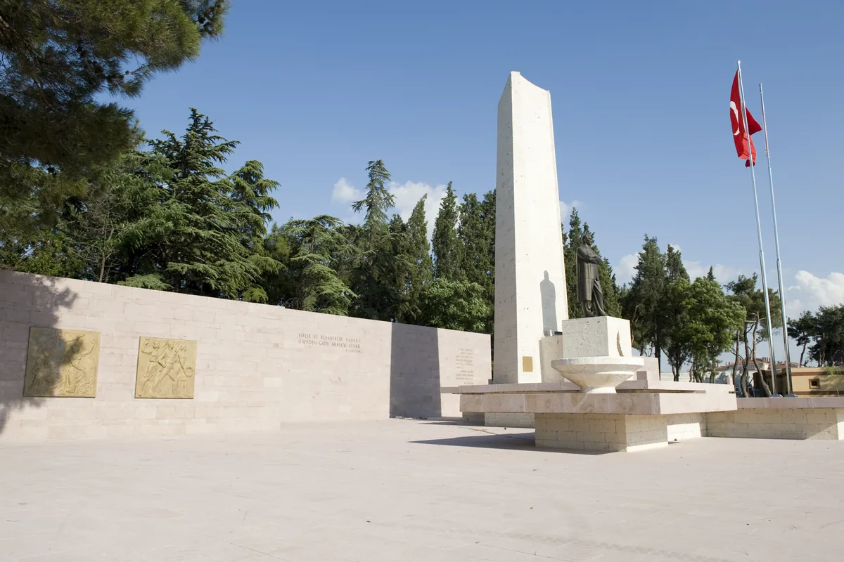 Altıeylül'deki Atatürk Anıtı'nın beyaz taş obeliski, Türk bayrağı ve çevresindeki çam ağaçları