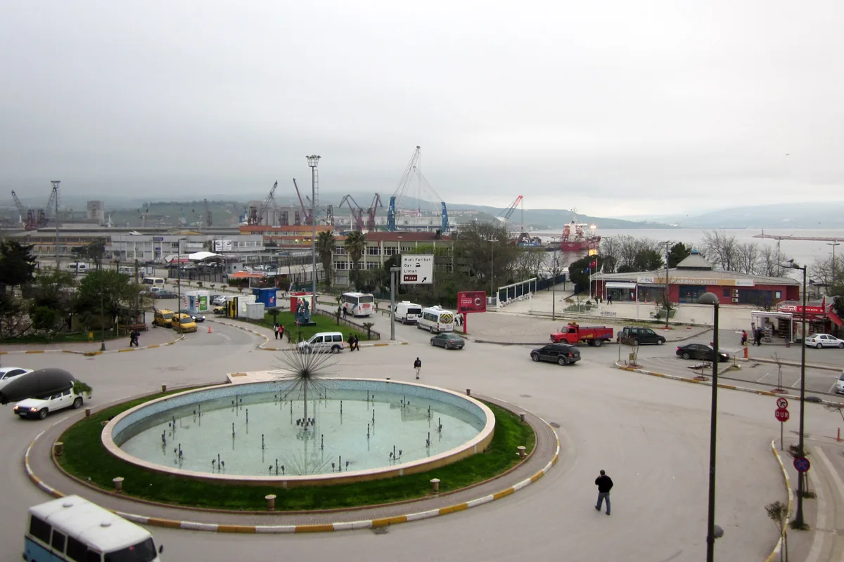 Bandırma limanı çevresinde vinçler, meydan çeşmesi ve araçlar; arka planda körfez