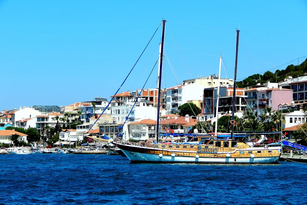 Çeşme 16 Eylül Mahallesi kıyısında demirlemiş yelkenli tekne ve arka planda şehir