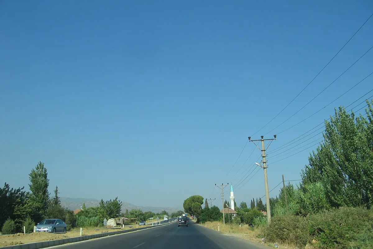 Aydın-Denizli karayolu (D320) üzerinde açık gökyüzü, uzakta dağlar ve bir köy minaresi, Sultanhisar sınırında