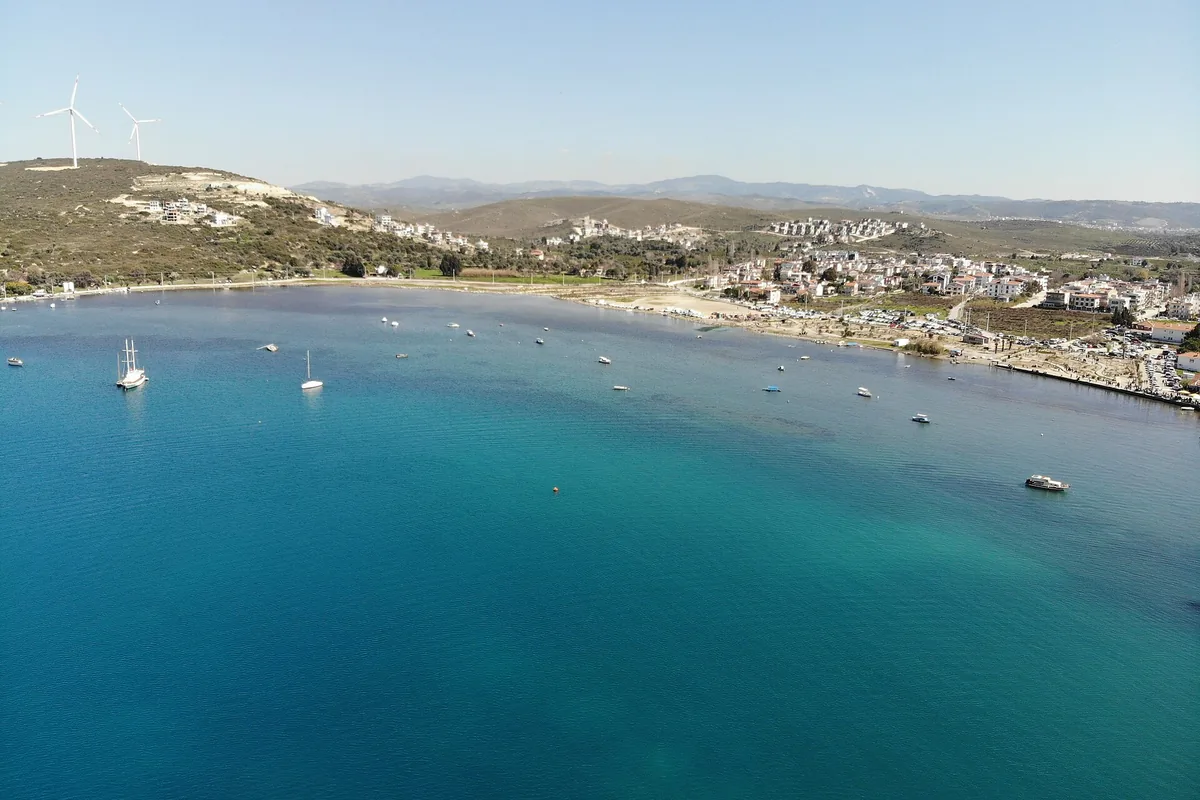 Sığacık koyunda turkuaz deniz, yelkenliler ve sırttaki rüzgar türbinleri